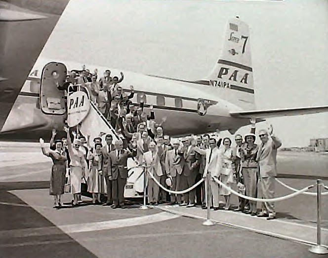 1950s Customers pose and wave on the ramp next to a Pan Am DC7  Clipper.